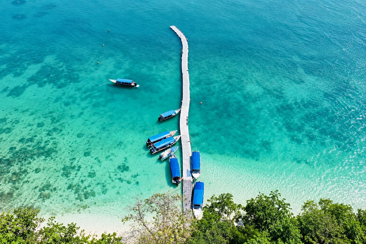 Aerial view of a Langkawi island jetty and blue-canopy speedboats in clear water