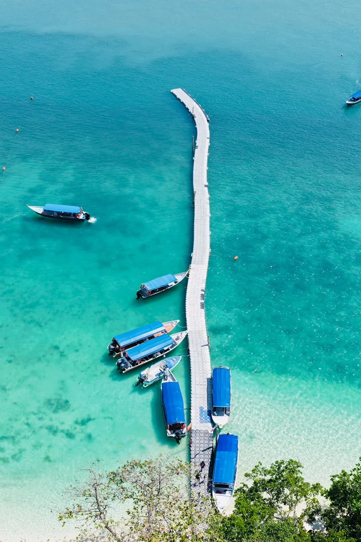 Aerial view of a Langkawi island jetty and blue-canopy speedboats in clear water