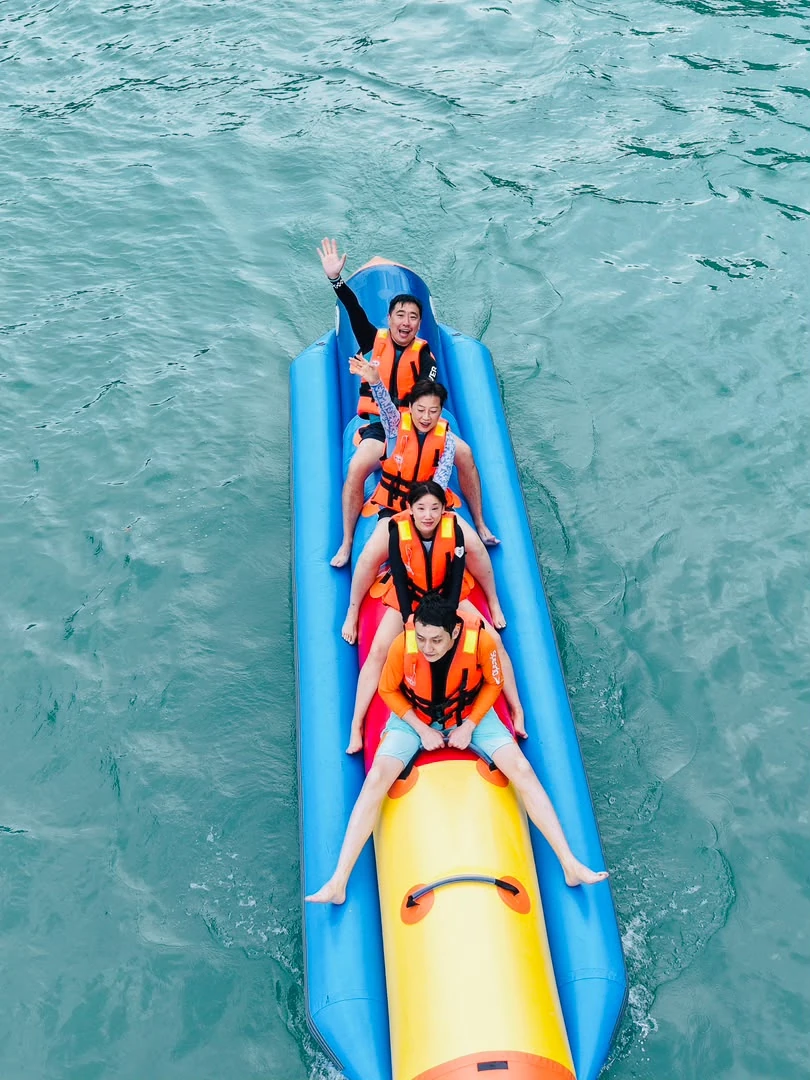 Four guests wearing orange life jackets on a blue and yellow banana boat