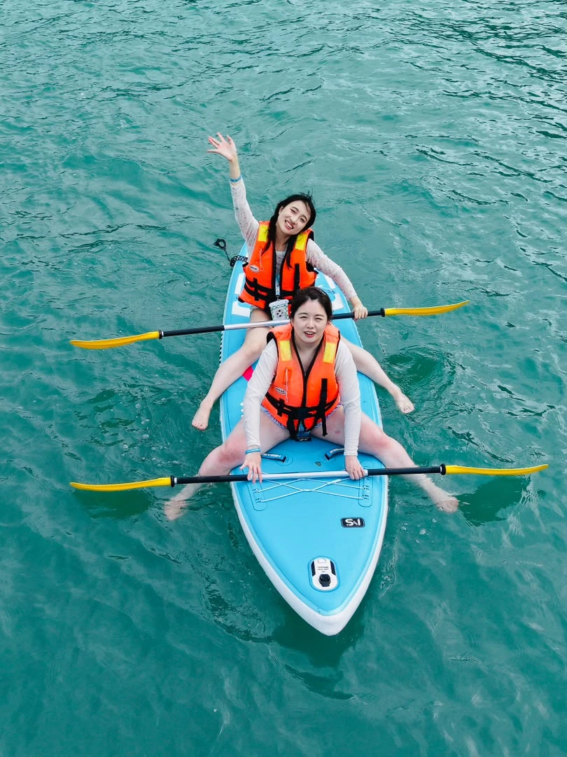 Two guests wearing life jackets seated on a blue paddleboard with paddles